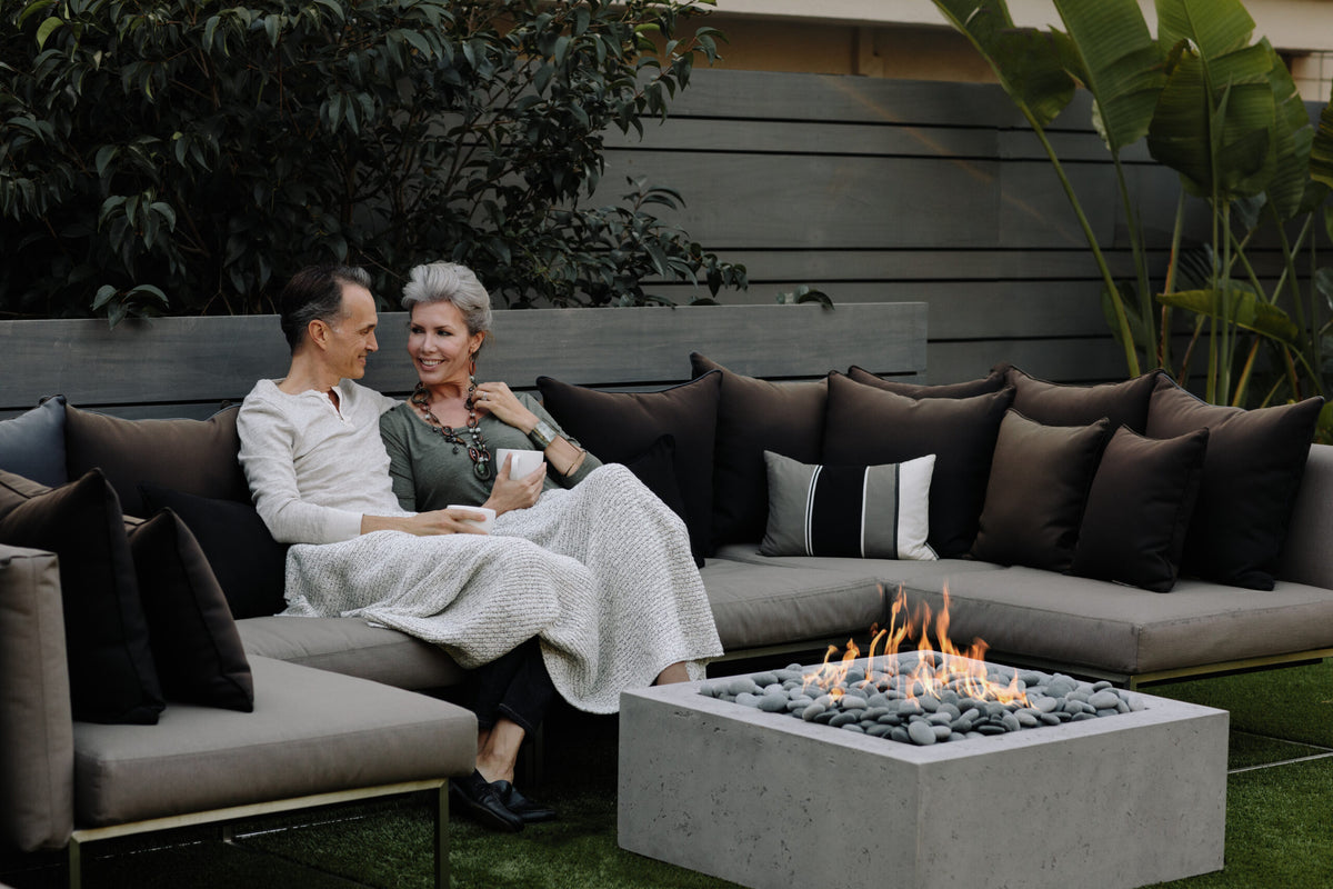 Two people sitting on a outdoor sofa with a fire pit table in the foreground