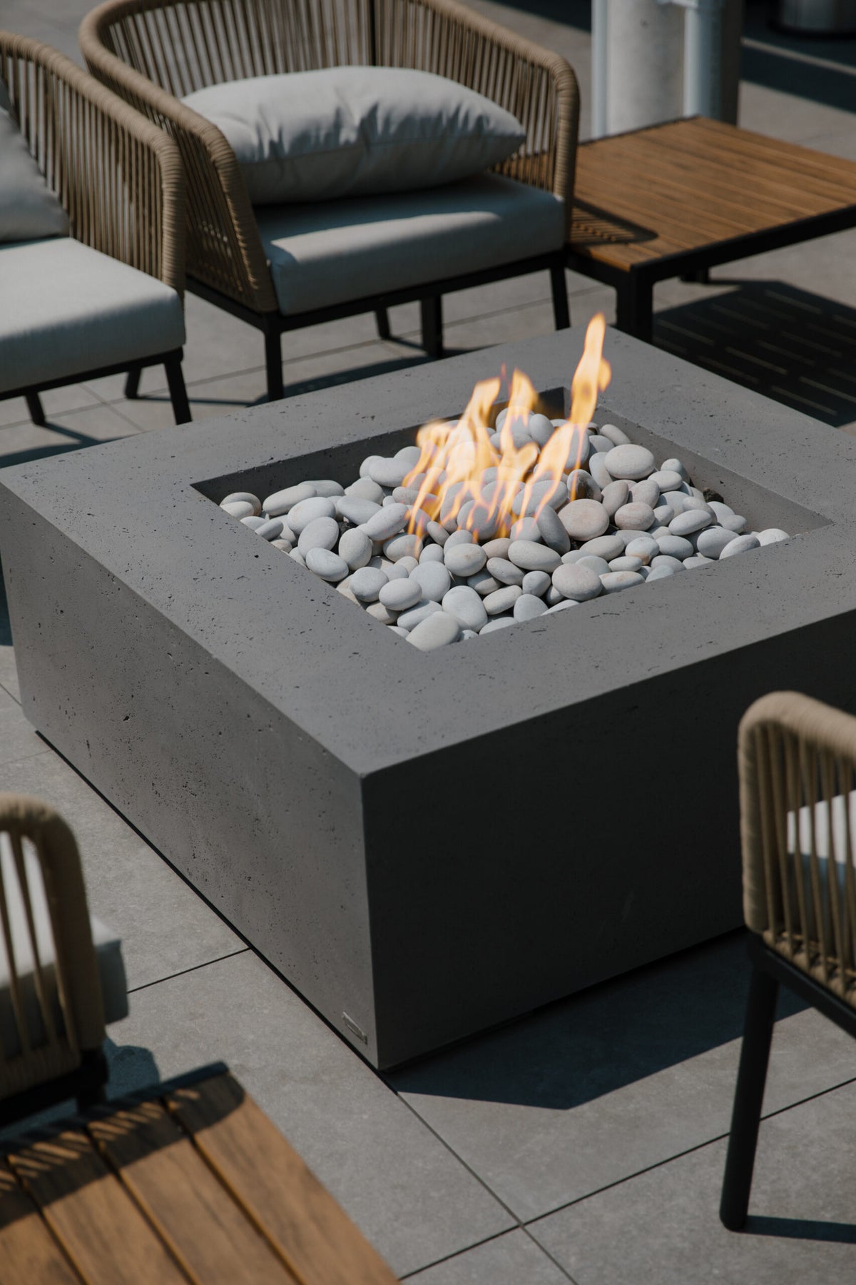 Fire pit table with flames surrounded by chairs on a patio