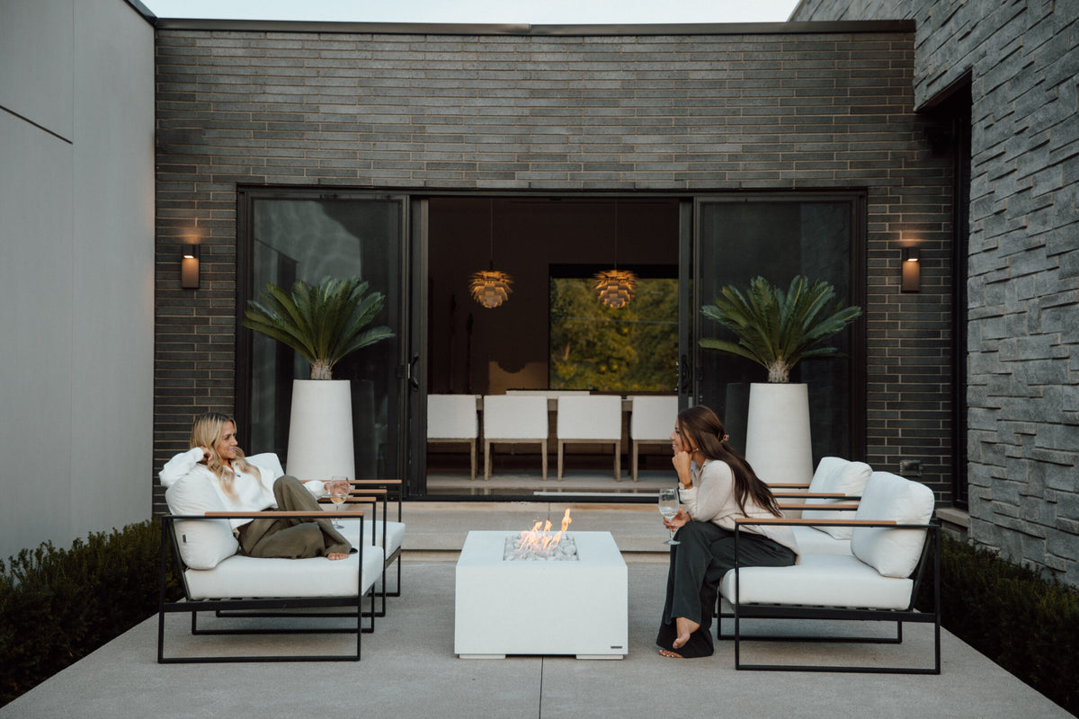 Two people sitting on outdoor furniture near a fire pit in a modern patio setting.