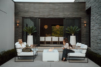 Two people sitting on outdoor furniture near a fire pit in a modern patio setting.